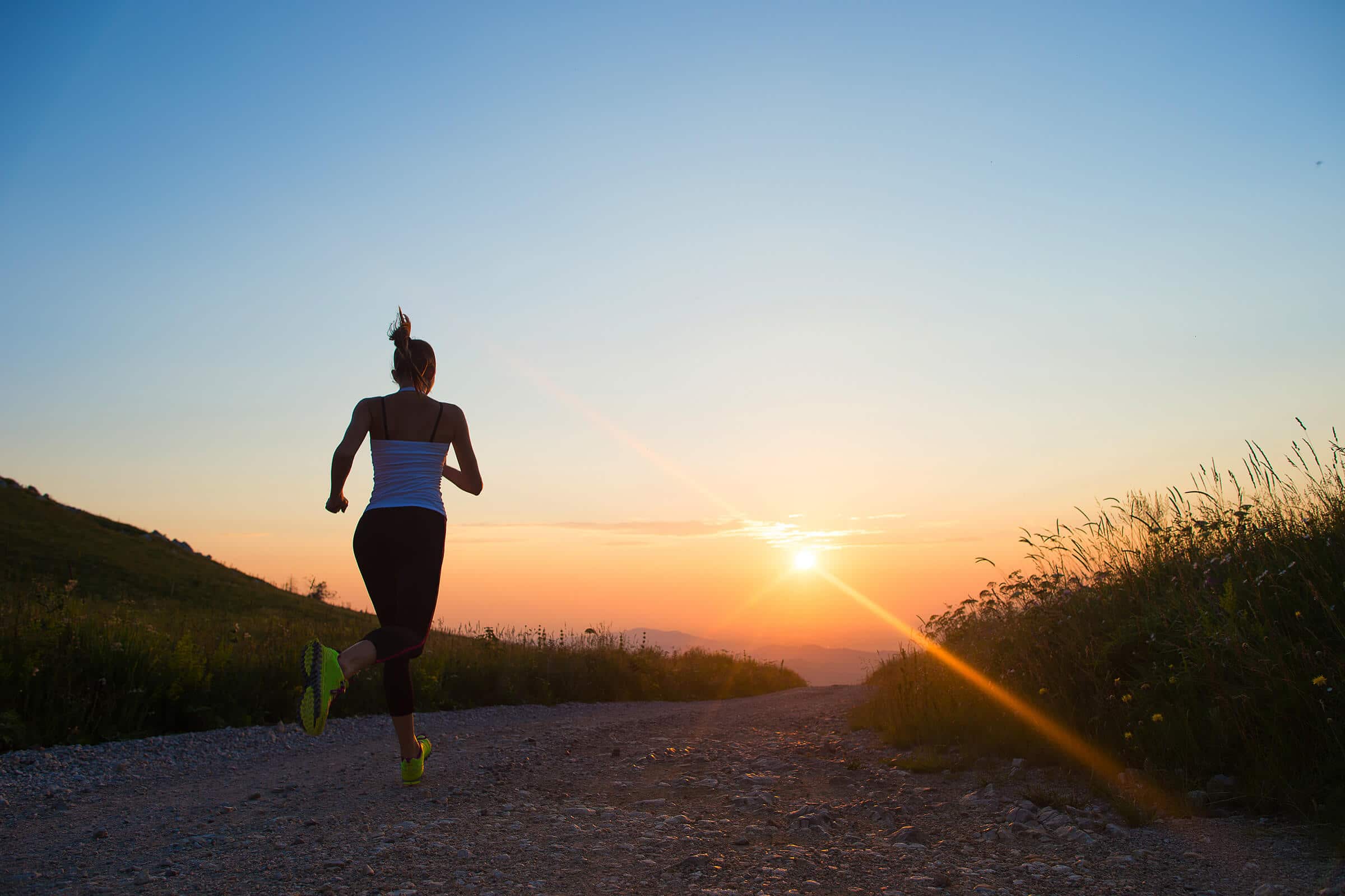 woman running outdoor on a mountain road at summer sunset